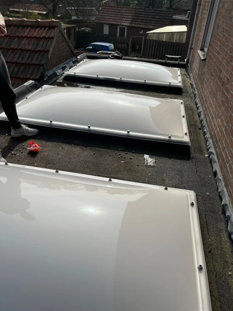 Drie lichtkoepels op een plat dak tussen rijtjeswoningen in Ede
