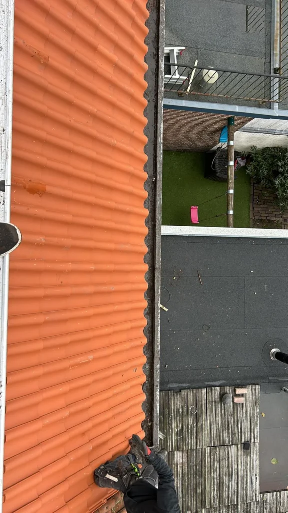 Dakgoot tussen een oranje pannendak en een plat dak van bovenaf in Ede